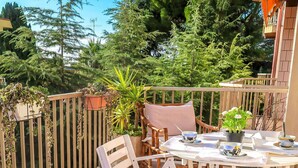 Eine Holzterrasse mit rundem Tisch und weißen Stühlen, umgeben von Kübelpflanzen und einem Holzzaun.