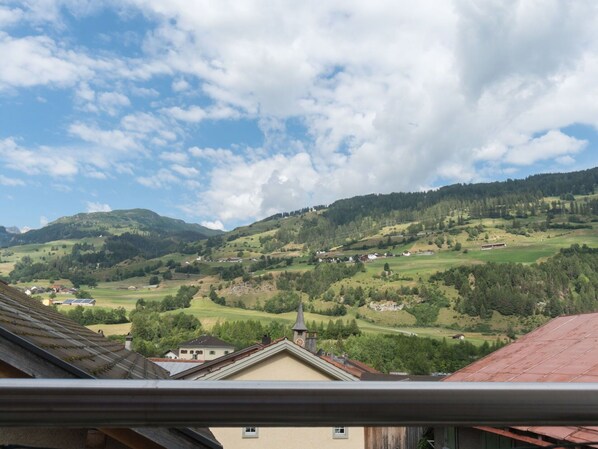 Vista de un valle con casas e iglesia, rodeado de colinas verdes y un cielo parcialmente nublado.
