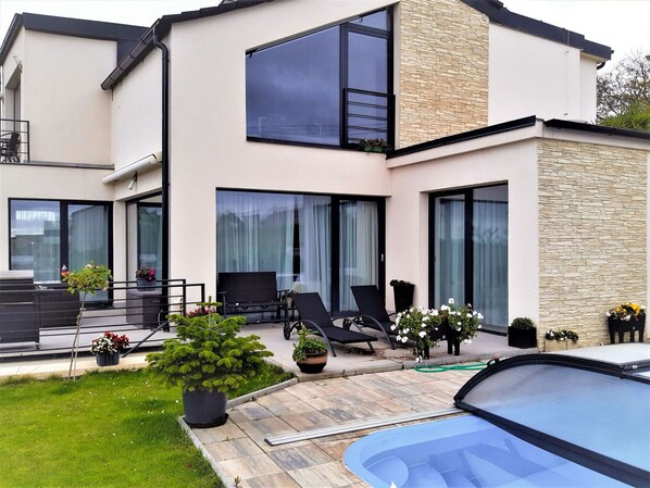 A modern two-story house with a patio, outdoor seating, and a swimming pool.