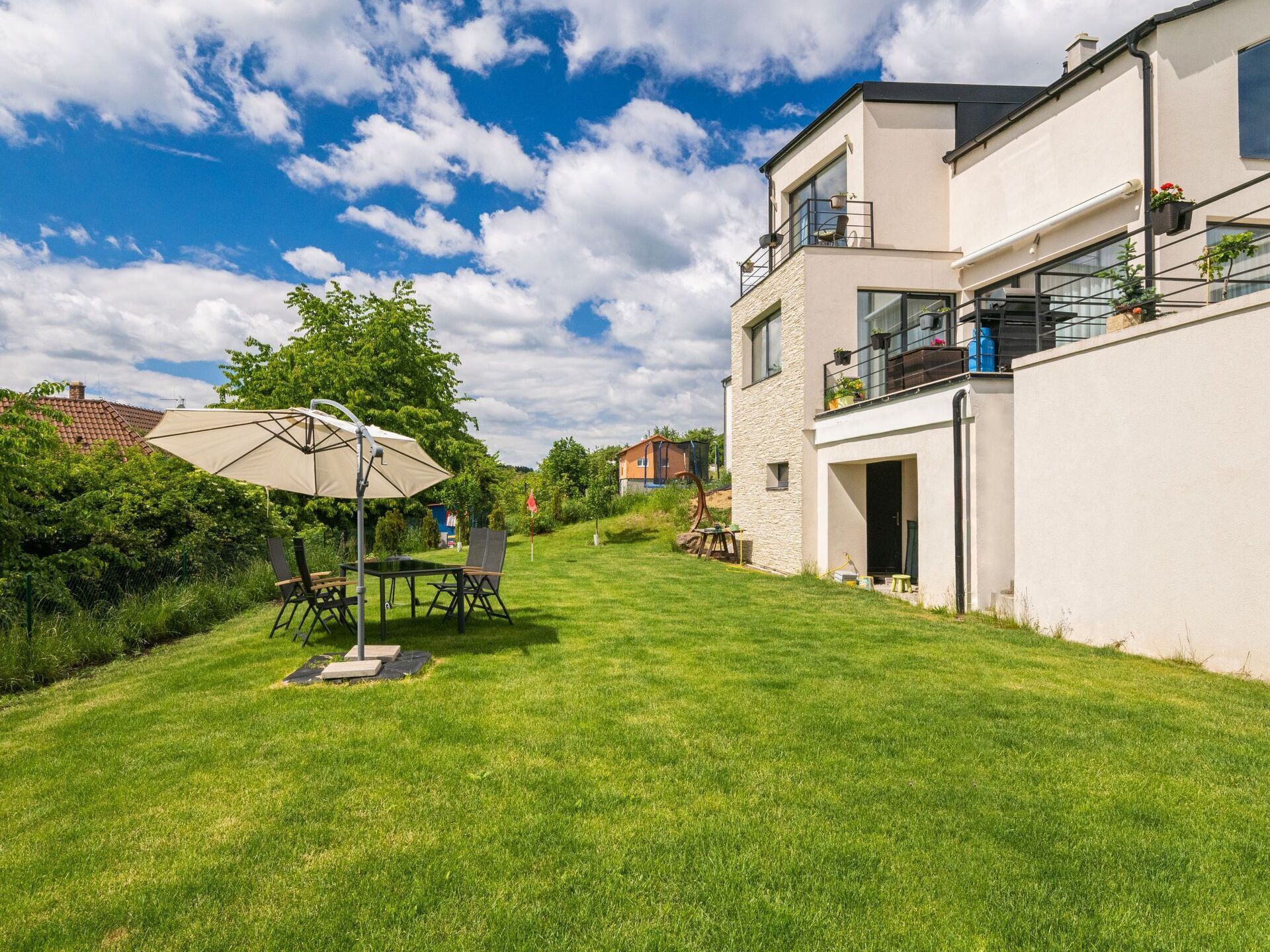 A modern two-story house with a well-maintained lawn, outdoor furniture, and a large umbrella.