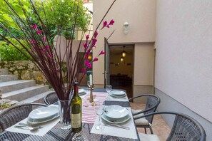 Un espace extérieur aménagé pour les repas, avec une table dressée pour deux personnes, entourée de chaises en osier.