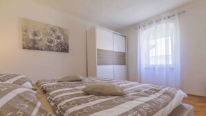 Ein Schlafzimmer mit Bett, Kleiderschrank, einem Gemälde und einem Fenster mit Vorhängen.
