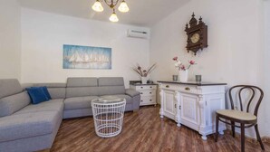 Ein Wohnzimmer mit grauem Sofa, einem kleinen runden Tisch, einem weißen Schrank und einem Holzsessel.