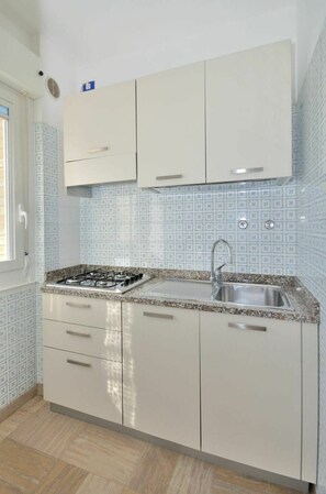 Compact kitchen with gas stove, sink, and countertop, featuring light-colored cabinetry and a decorative backsplash.