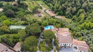 Eine Vogelperspektive auf ein Anwesen mit Swimmingpool, Tennisplatz und üppiger, umliegender Bepflanzung.