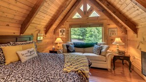 Une chambre dans une cabane en rondins, avec un lit en mezzanine, un canapé et une cheminée.
