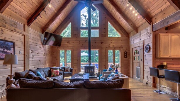 L’intérieur d’une cabane en rondins, avec un plafond haut, des murs en bois, une cheminée, un canapé et un téléviseur.