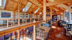 Un vaste espace à manger agrémenté de poutres en bois, doté d’une mezzanine et offrant différents types d’aménagements pour s’asseoir.