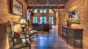 L’intérieur d’une cabane en rondins, avec un canapé, des fauteuils, une table et une cheminée.