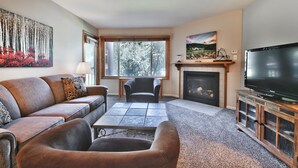 Ein Wohnzimmer mit Sofa, Sessel, Couchtisch, Kamin, Fernseher und Kunstwerken.