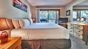 Ein Hotelzimmer mit einem großen Bett, einem Fernseher, einer Holzkommode und einem Bild an der Wand.