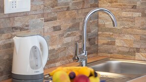 A kitchen with a stainless steel sink, a white kettle, and a bowl of fruit on the counter. - Apartments Njirić - Family Studio with Balcony Sea View - No.2 (Zaton)
