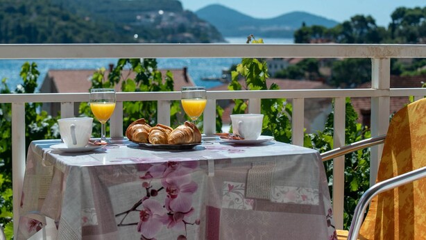 A table with croissants, orange juice, and a cup on a balcony overlooking a scenic view of hills and water. - Apartments Njirić - Family Studio with Balcony Sea View - No.2 (Zaton)