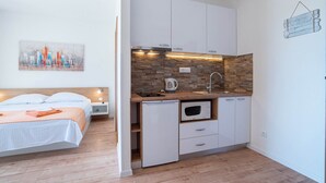 A compact hotel room with a bed, a kitchenette, and a cityscape painting. - Apartments Njirić - Family Studio with Balcony Sea View - No.2 (Zaton)