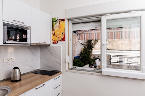 Una cocina moderna con microondas integrado, tetera y ventana con vistas a un balcón.