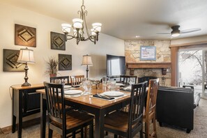A dining area with a chandelier, stone fireplace, and a television.