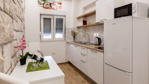 Una cocina moderna con armarios blancos, un microondas y un refrigerador. Hay una ventana con persianas, un fregadero y una encimera con un hervidor.