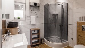 Un baño moderno con ducha envuelta en vidrio, lavamanos blanco y tocador de madera.