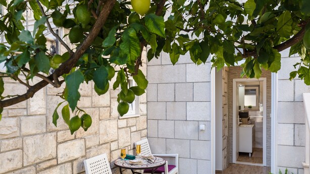 Un pequeño espacio al aire libre con dos sillones blancos de mimbre, una mesa redonda, un muro de piedra y una puerta que da a un baño.