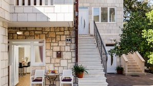 A stone building with a staircase leading to a second floor. There are two white chairs and a table outside, with a potted plant nearby. - Apartments Martha-Superior Studio No.3 (Dubrovnik)