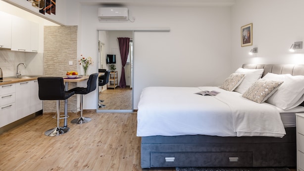 A modern hotel room with a bed, bedside table, and a small desk with a chair. There is a kitchen area with cabinets and a sink. - Apartments Martha-Superior Studio No.3 (Dubrovnik)