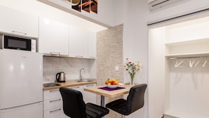 A modern kitchen with white cabinets, a microwave, a kettle, and a fruit bowl on the counter. There are two black chairs and a small table with a vase of flowers. - Apartments Martha-Superior Studio No.3 (Dubrovnik)