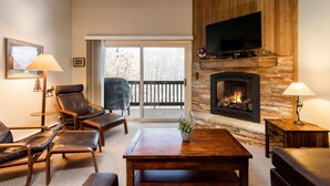 A living room with a fireplace, leather furniture, a television, and a view through a glass door.