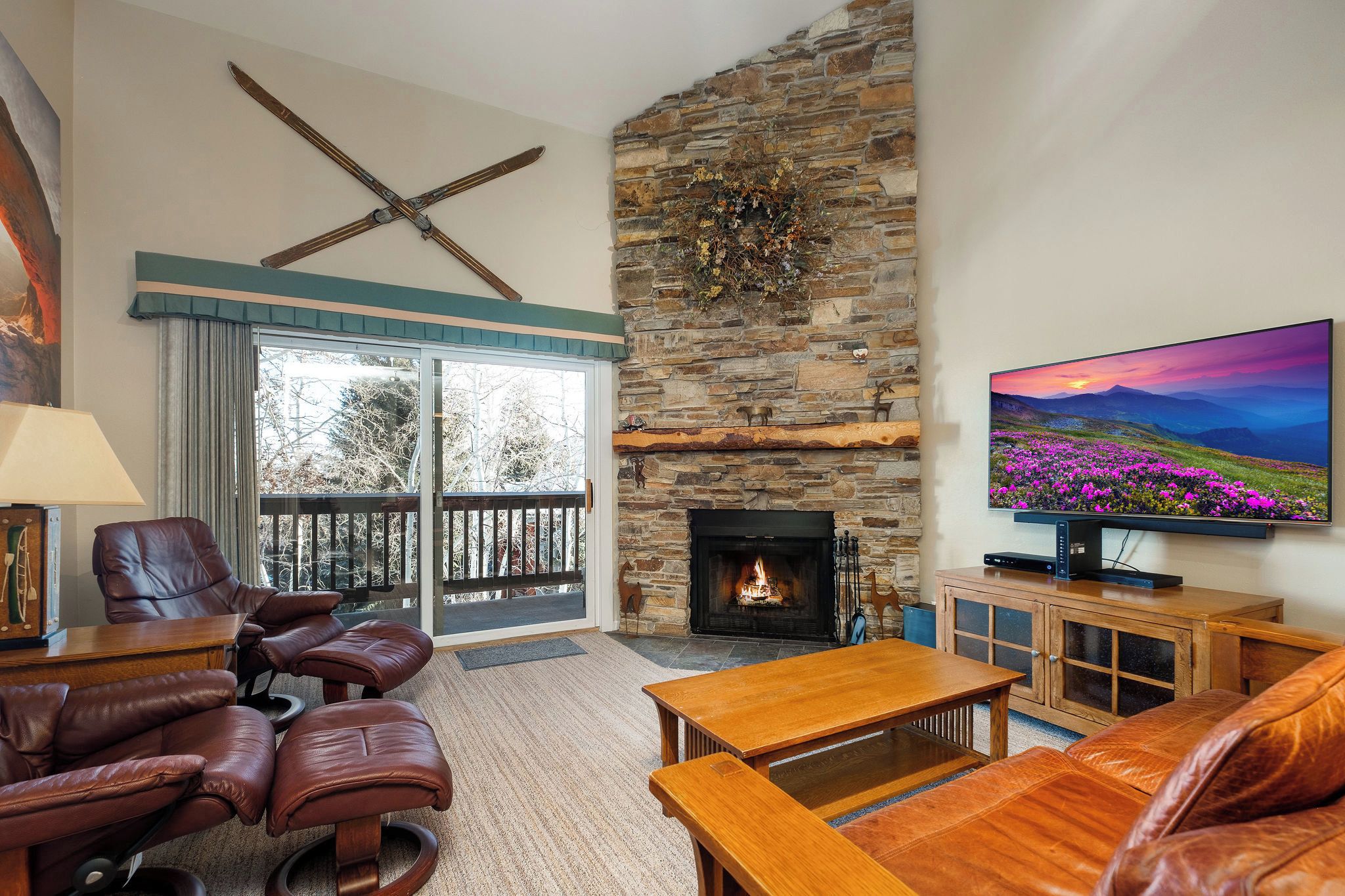 A living room with a stone fireplace, leather furniture, a television, and a balcony with a view.