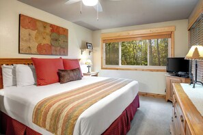 Une chambre avec un grand lit, une télévision, une fenêtre donnant sur des arbres et un tableau accroché au mur.