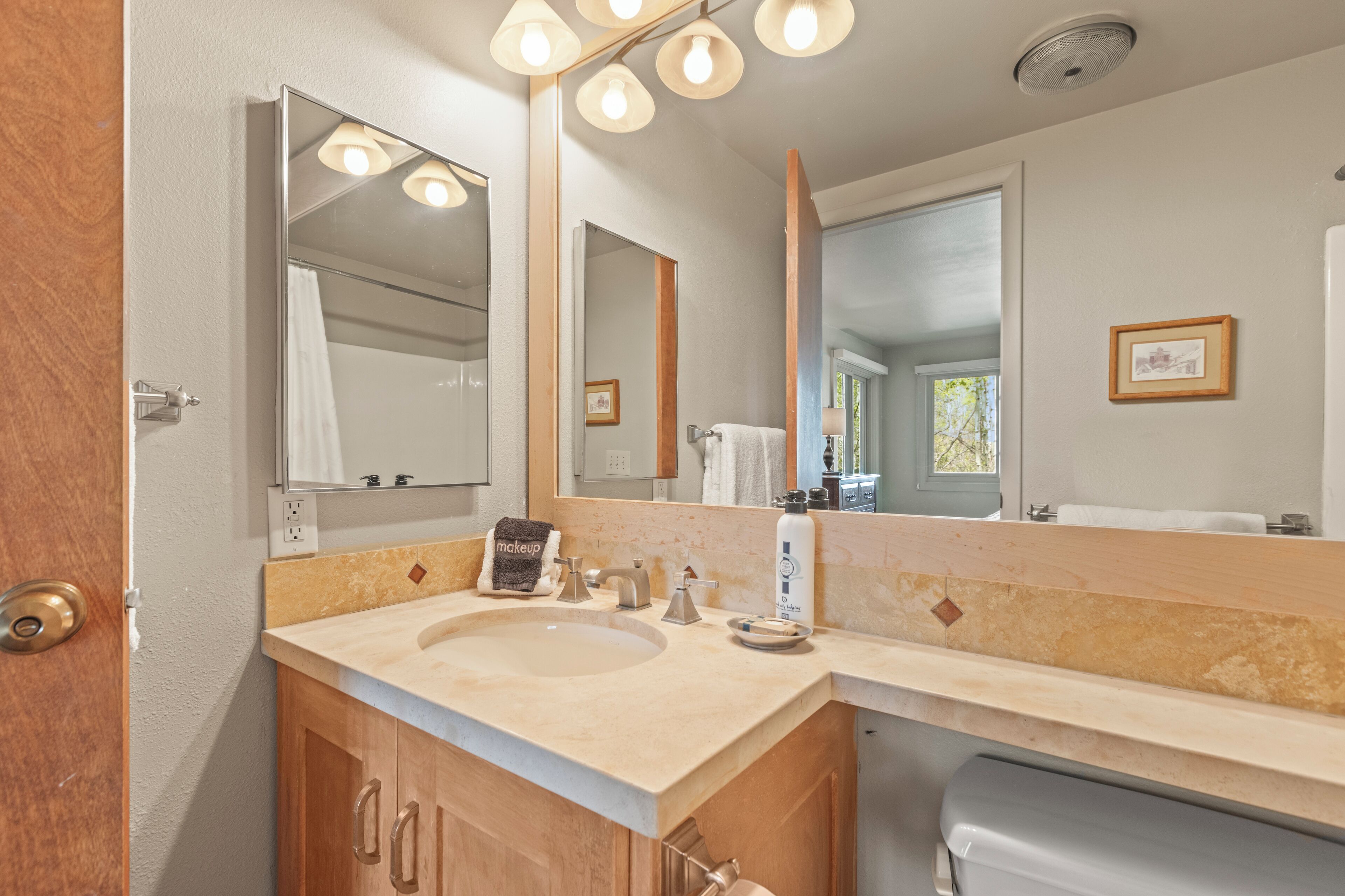 Un baño con un lavabo color beige, armarios de madera, un espejo grande y un perchero para toallas.