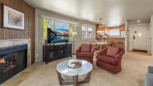 A living room with a fireplace, a television, a round coffee table, and red armchairs.
