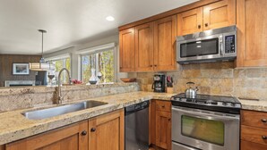 A kitchen with wooden cabinets, stainless steel appliances, granite countertops, and a window with a view of trees.