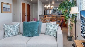 A living room with a sofa, a dining table, chairs, a chandelier, and a potted plant.