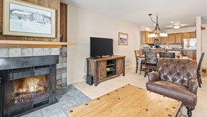 A living room with a fireplace, a television on a wooden stand, a leather armchair, and a dining area with a chandelier. - Managed by Park City Lodging-True Ski-In/Ski-Out to Park City Mountain Resort! (Park City)