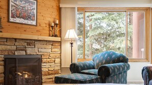 A cozy living room with a stone fireplace, a large window with a forest view, and a patterned armchair. - True Ski-In/Ski-Out to Park City Mountain Resort I Managed by Park City Lodging (Park City)