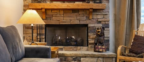 A cozy living room with a stone fireplace, a framed picture above it, and a decorative bear statue.