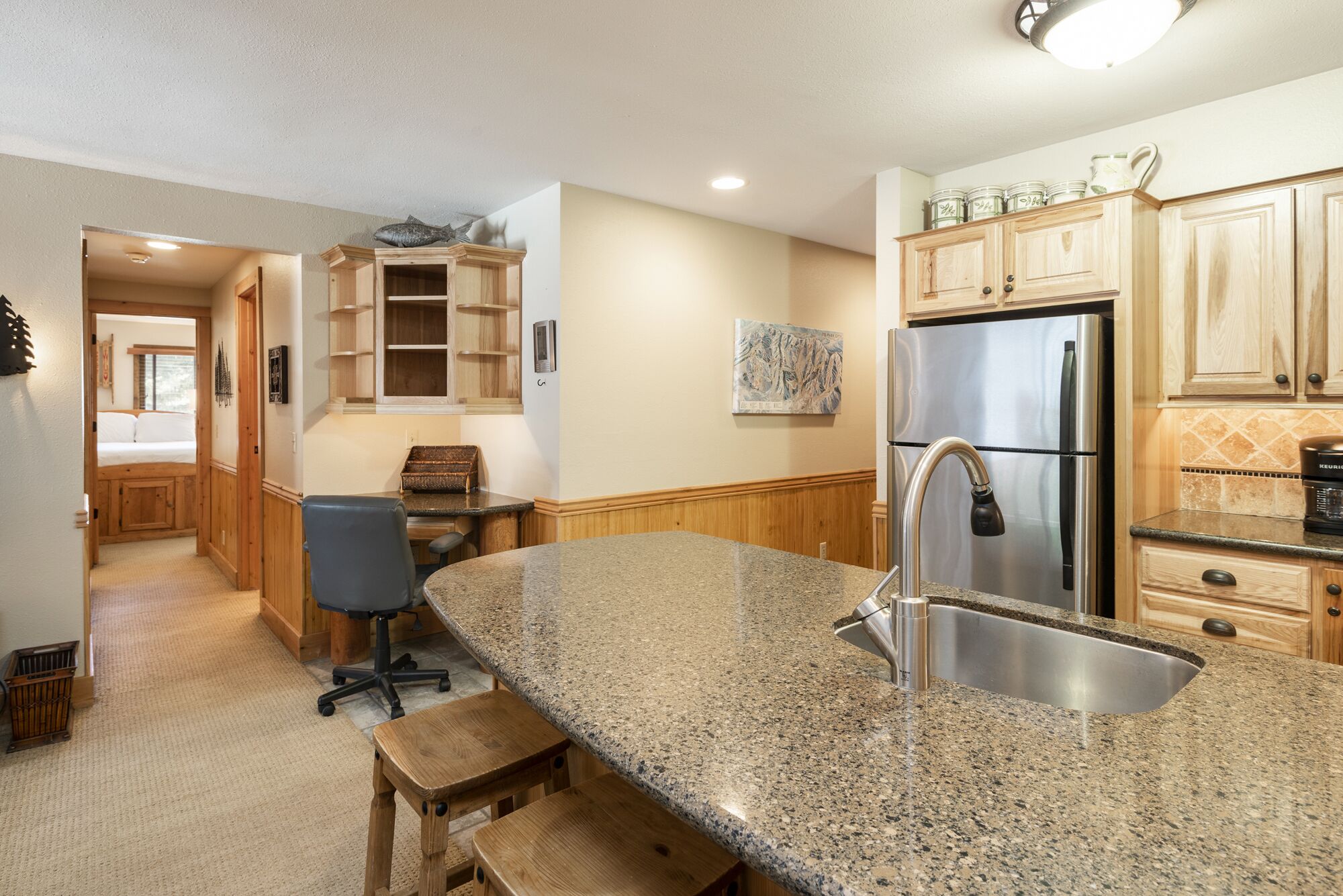 A kitchen with granite countertops, a stainless steel refrigerator, wooden cabinets, and a built-in bench.