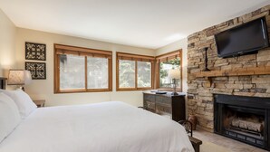 Une chambre avec un grand lit, une cheminée en pierre et un téléviseur fixé au mur.