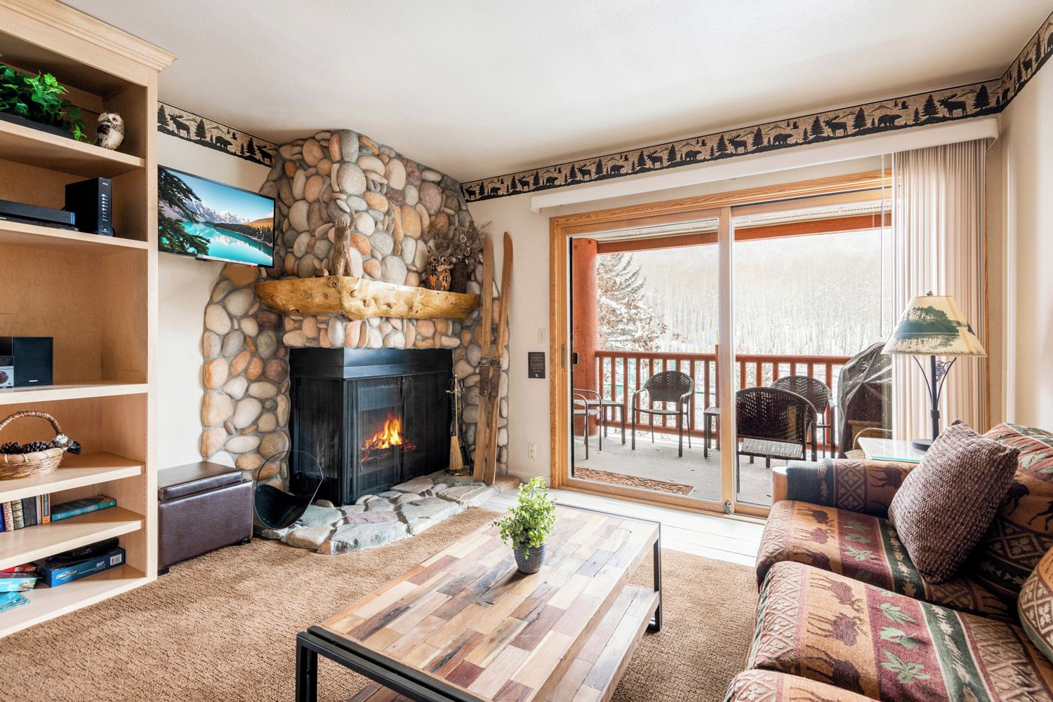 A cozy living room with a stone fireplace, a sofa, a coffee table, and a bookshelf.