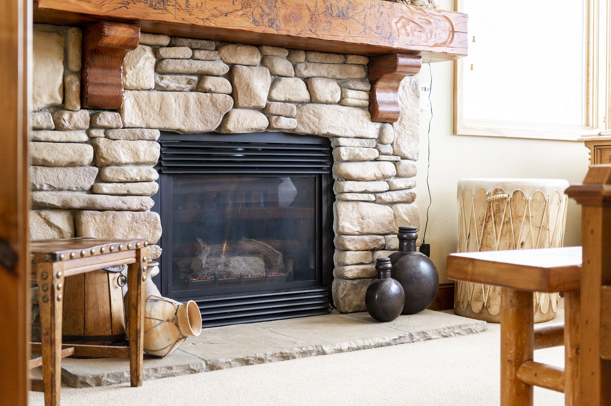 A stone fireplace with a black screen, surrounded by rustic wooden furniture and a large vase.