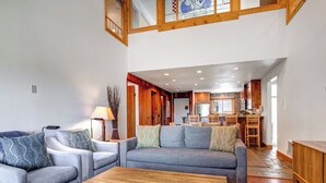 A spacious living room with a grey sofa set, a wooden coffee table, and a view of the kitchen and dining area through an open doorway.