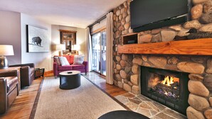 Un salón acogedor con chimenea de piedra, un televisor de pantalla plana montado arriba y un área de estar cómoda con sofá y mesa de centro.
