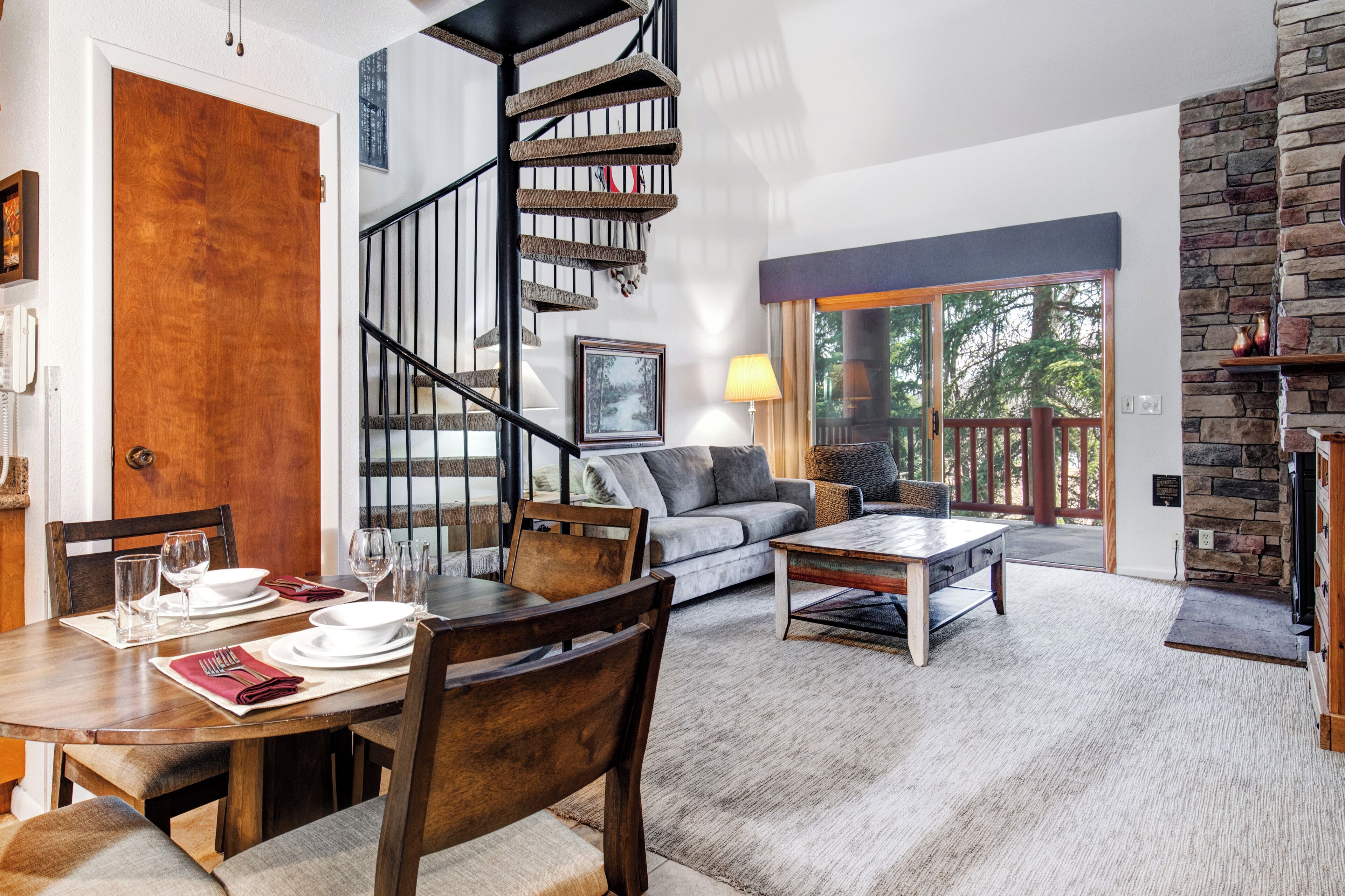 A dining area with a wooden table set for four, a sofa, and a staircase.