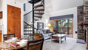 Un comedor con una mesa de madera dispuesta para cuatro personas, un sofá y una escalera.