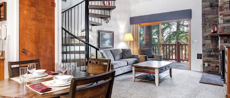 A dining area with a wooden table set for four, a sofa, and a staircase.