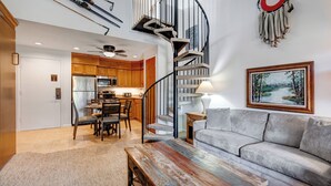 Un espacio habitable amplio con una mesa de centro de madera, un sofá gris y una escalera espiral que conduce a un nivel superior.