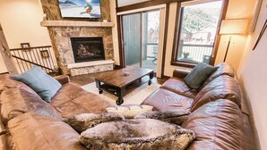 Ein gemütliches Wohnzimmer mit Kamin aus Stein, einer Ledersofa und einem darüber montierten Fernseher.