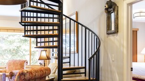 A spiral staircase with a wooden finish, a lamp, and a patterned armchair in a room with a window and a bed. - Managed by Park City Lodging-True Ski-In/Ski-Out to Park City Mountain Resort! (Park City)