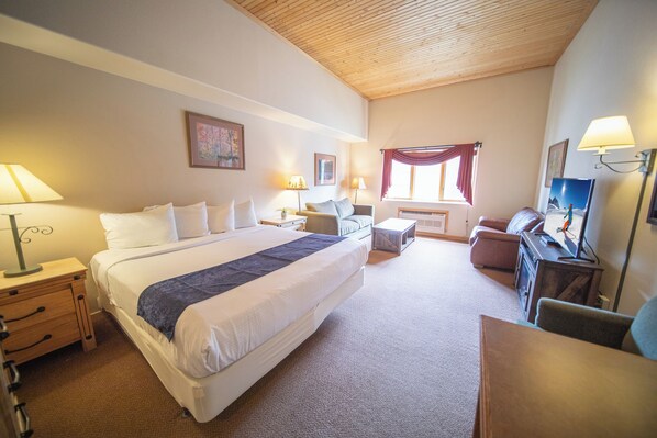 Habitación de hotel con una cama grande, mesitas de noche, un escritorio, una silla, televisor y ventana con cortinas.
