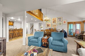 A spacious living room with a high ceiling, a wooden staircase, and a dining area with wooden chairs and a table.